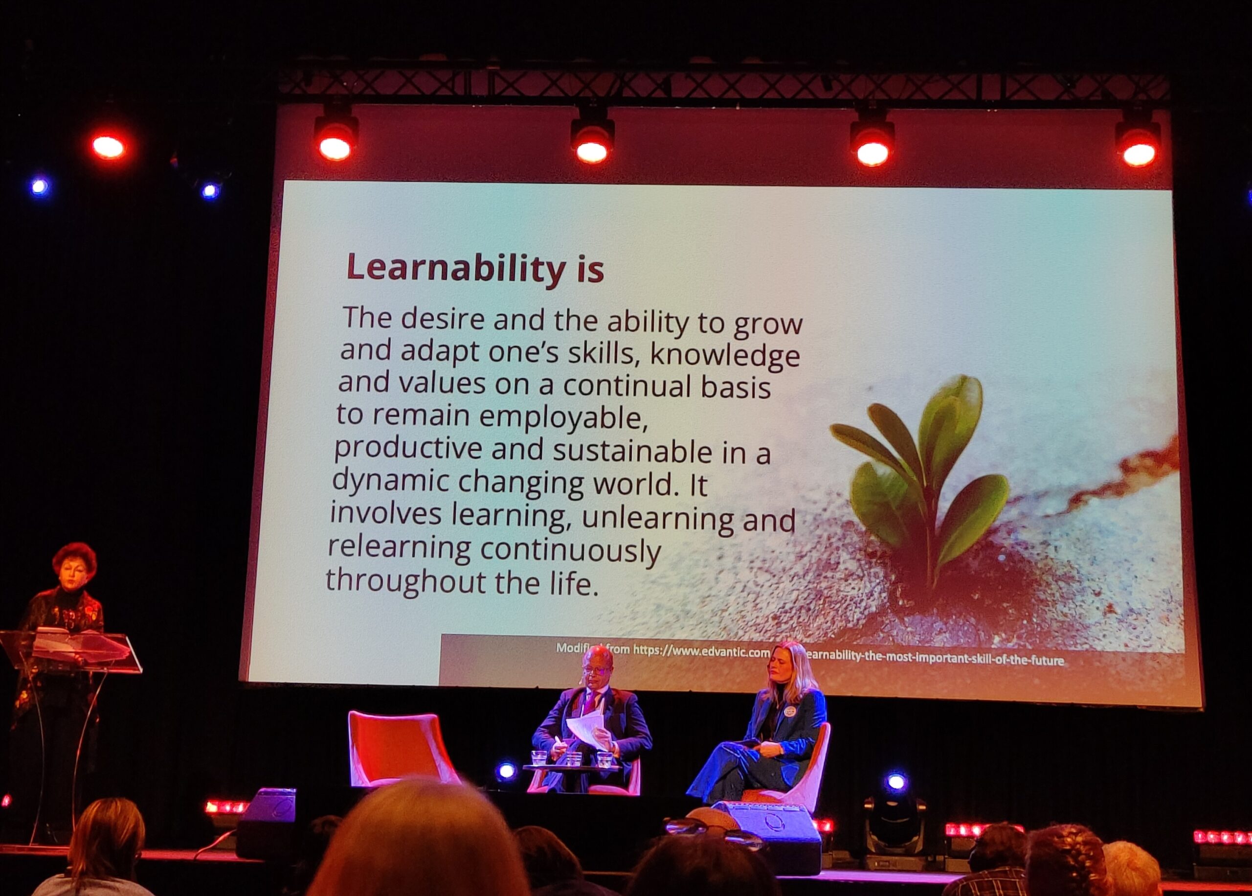 Foredragsholder Asha Kanwar, President and CEO Commonwealth of Learning, på scenen med en slide fra sin presentasjon. På det bildet står det: Learnability is The desire and the ability to grow and adapt one\s skills, knowledge and values on a continual basis to remain employable, productive and sustainable in a dynamic changing world. It involves learning, unlearning and relearning continuously throughout the life.